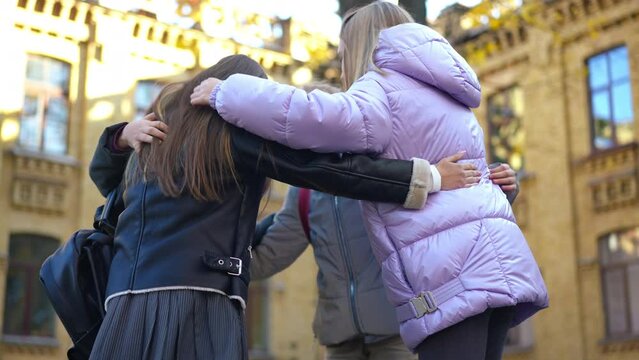 Group of cheerful teen classmates standing in circle talking hugging and laughing on schoolyard on autumn day. Happy confident Caucasian girls and boy meeting before classes outdoors. Friendship