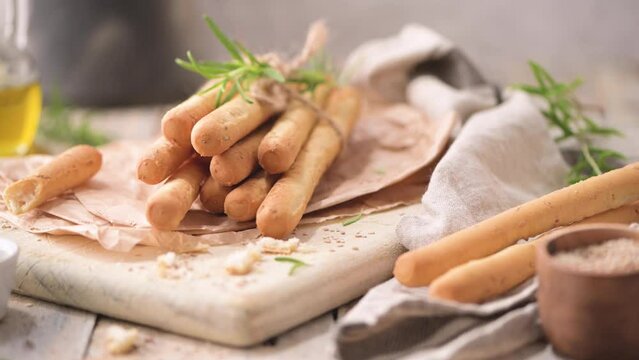 Traditional italian breadsticks grissini with rosemary, olive oil and sesame seeds on wooden countertop.