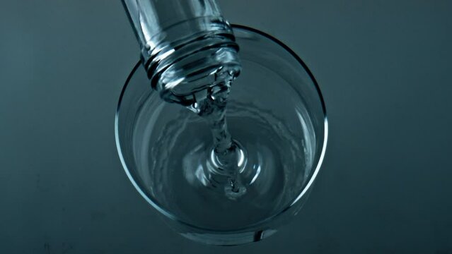 Bottle pouring pure water into transparent cup closeup. Top view liquid filling