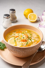 Italian lemon chicken orzo soup in bowl on concrete background