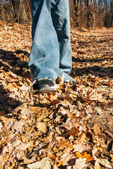 Leg of a girl in a sneaker and jeans, against the background of autumn yellow fallen leaves on the ground. Autumn season