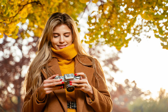Young pretty girl analog photography enthusiast, taking pictures in the park in autumn  