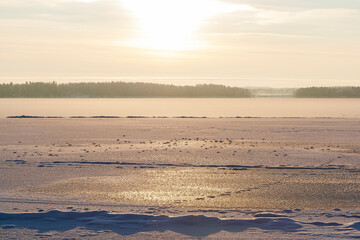 Sun shining above a frozen and snowy lake in Finland in the winter. Wintry, sunny and serene landscape at morning.