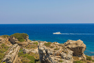 Beautiful view of natural landscape with passing sailing yacht on rocky coastline on endless surface of blue sea water on horizon. Greece.