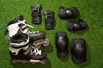 Flat lay composition with inline skates and protective pads on green grass background.
