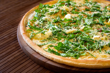 Pizza with cheeses and herbs on a wooden plate. Close-up, selective focus