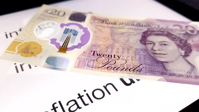 Great British sterling twenty pound bank notes falling one after another slowly onto a white digital screen with the words inflation rates calculator displayed.