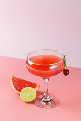 Fresh grapefruit juice in a glass with grapefruit slices, lime and cherry on a pink background. Copy spase