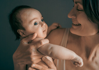 Mom, mummy, young mother with little baby daughter. Mum kissing and hugging child. Newborn cute happy girl smiling in woman hands. Happiness for parents in family. Aged parents, parenting, motherhood