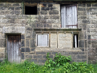 derelict abandoned old stone house with broken window and shabby wooden door overgrown with weeds