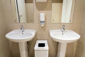 Ceramic sinks in a public toilet with a soap dish and a wastebasket