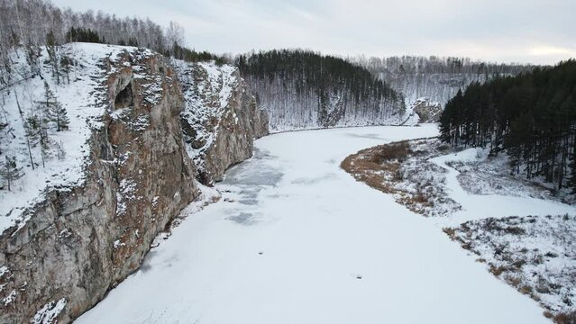 takeoff over the winter river covered with ice, rocky shores and a frozen river. aerial view, drone footage