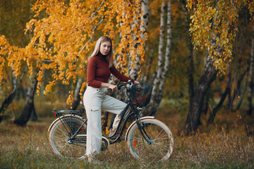 Fototapeta na wymiar Happy active young woman riding bicycle in autumn park.