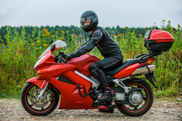 Fototapeta na wymiar Young handsome man in black helmet on large red motorcycle.