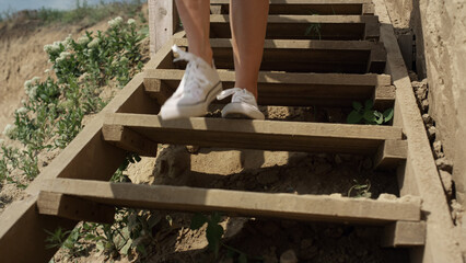 Slim girl legs running down beach staircase wearing white sneakers close up.