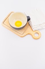 tazza rustica in terracotta con rosso d'uovo, tagliere in legno e canovaccio su tavolo bianco, vista dall'alto