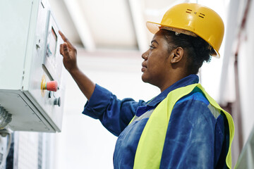 Young serious African American female engineer pressing button on panel to start machinery equipment during work in factory