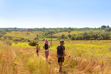 Three young boys with backpacks go hiking along the  field.