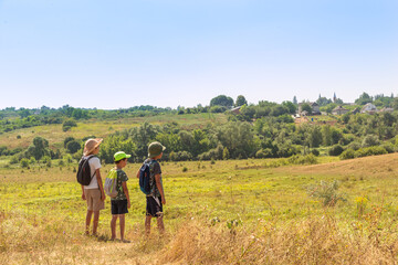 Naklejka na ściany i meble Three young boys with backpacks go hiking along the field.