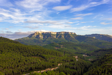 Landscape of a green forest with a large mountain in the center and clouds on top of it, and a road winding towards it