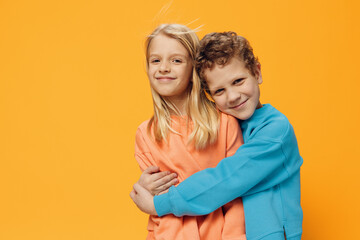 cute, joyful, loving school-age children stand on a yellow background and gently hug each other. theme of friendship and relationships