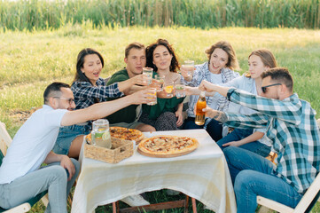 Group of friends are relaxing together outdoor. Young cheerful people clink glasses and laugh.