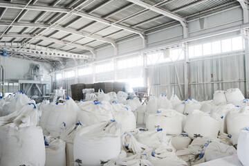 Part of spacious warehouse or storage room with heaps of huge white sacks containing loose raw materials for industrial production