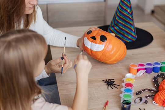 mother and little kid daughter making jack-o-lanterns together while preparing for halloween party.