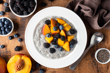 Chia pudding bowl with peach and blueberries on wooden table background, top view
