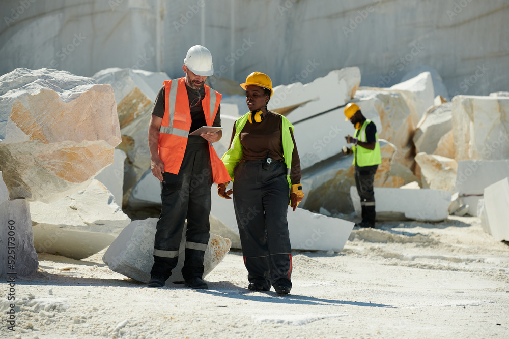 Poster two young intercultural workers of marble quarry discussing online manual guide while standing again