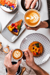 Fototapeta na wymiar Personas sosteniendo dos tazas de café, al fondo una mesa con postres.