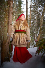 Little girl in old peasant clothes including a fur coat and a shawl in a cold winter forest with...