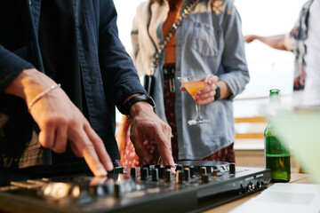 Hands of young male deejay rotating turntables while creating dance music for people enjoying rooftop party on terrace of outdoor cafe