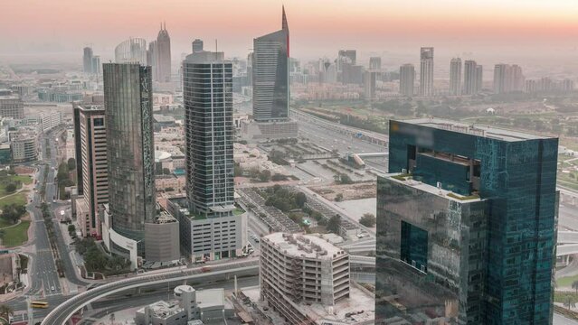 Aerial view of media city and al barsha heights district area night to day transition timelapse from Dubai marina. Towers and skyscrapers with traffic on a highway from above