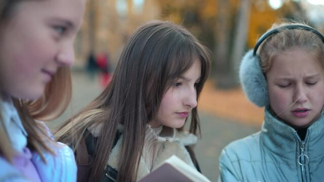 Panning left to right of curios concentrated teen girl discussing homework with classmates outdoors. Charming pretty Caucasian schoolgirl talking with friends studying on schoolyard
