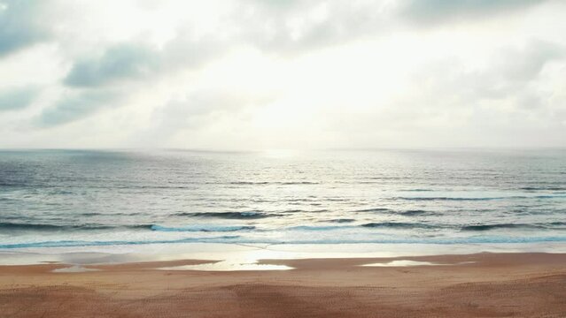 Static shot of cloudy sky and sand beach on ocean shoreline at sunset. Low tide with mild golden sun light High quality 4k footage from drone