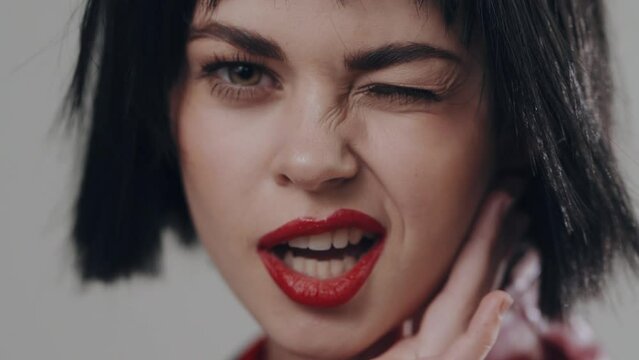 Closeup portrait of a woman who winks and shows her tongue while looking at the camera with a beautiful smile and red lips