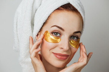 Close up face of adorable young woman in towel after shower, using golden collagen patches for...