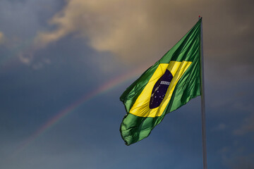 A bandeira do Brasil. Bandeira do Brasil voando, tremulando ao vento e com o céu e arco-íris ao fundo. - obrazy, fototapety, plakaty