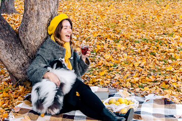 Portrait of a beautiful young woman in a yellow beret with her very affectionate dog in the forest. The dog wants to lick tea at a picnic. A pet on a walk