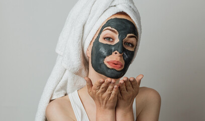 Portrait of smiling young woman with cosmetic mask on face blowing air kiss. Isolated over grey studio background.