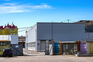 Naklejka premium Industrial area. Barrier gate at entrance to industrial area. Factory or factory checkpoint. Industrial area in summer weather. Hangar with gate. Two-story warehouse building behind barrier gate