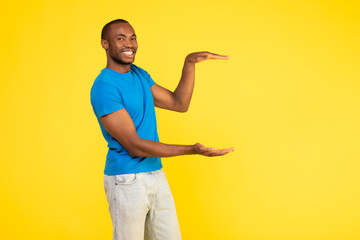 African American Male Holding Invisible Object In Hands, Yellow Background