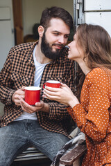 Young beautiful loving couple travelling across country in the van. Millennial man and woman in a travel camper. Cozy atmosphere, vacations vibe. Drinking tea, cooking marshmallow on a campfire
