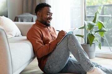 Cheerful Black Male Writing Taking Notes Sitting At Home