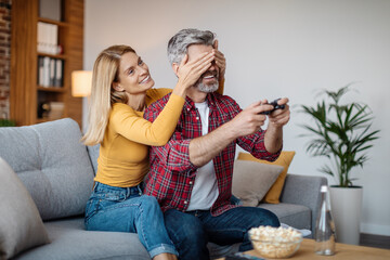 Cheerful mature caucasian lady closes eyes to man with joystick, interferes with online game in free time - obrazy, fototapety, plakaty