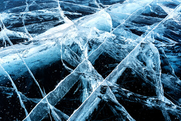 Transparent dark blue ice of frozen Baikal lake with white cracks pattern. Beautiful winter nature background.
