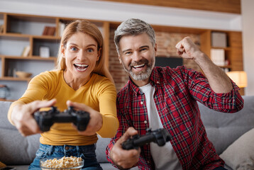 Glad excited adult caucasian female and male with joysticks play in online game in free time, celebrate victory © Prostock-studio
