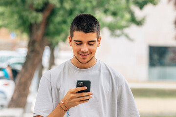 Fototapeta na wymiar smiling young man on the street looking at mobile phone or smartphone
