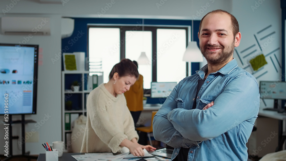 Poster portrait of confident man entering frame posing with arms crossed and smiling in busy startup office